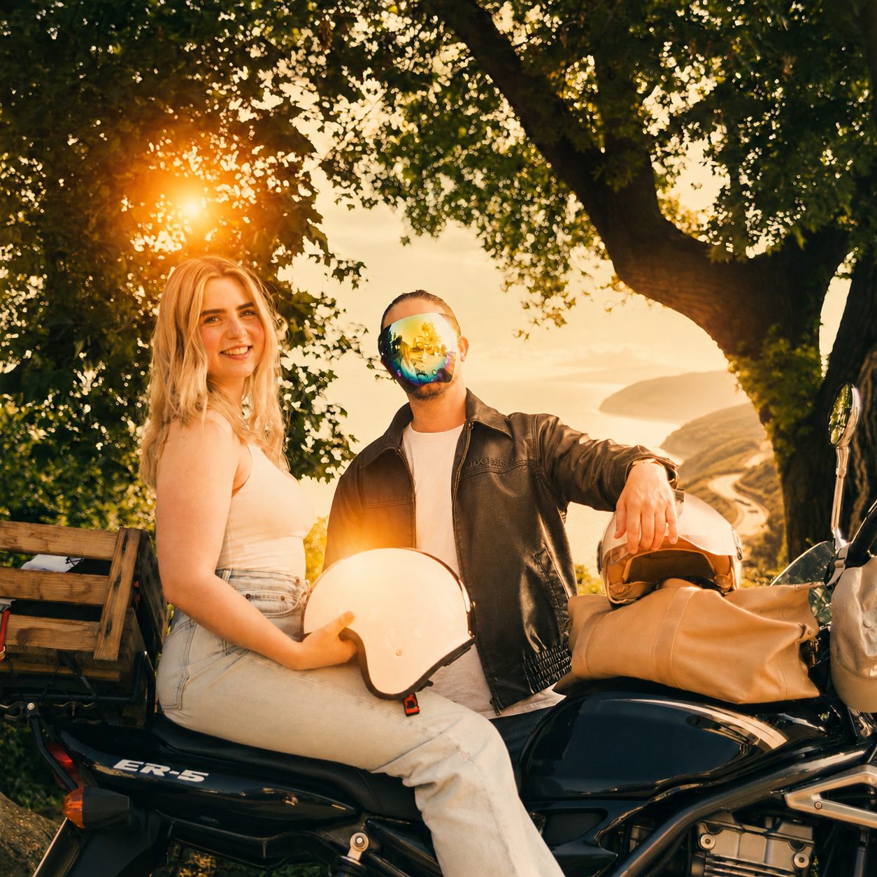 Ebba sitzt lächelnd auf einem Motorrad im Sonnenuntergang, Vlyon steht mit verspiegeltem Face Shield daneben.